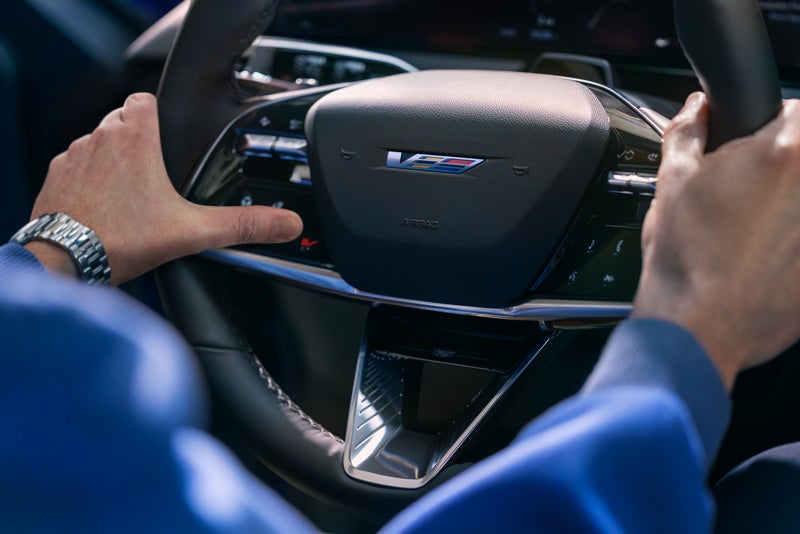 Close-up of a Man About to Press the V-Button on the 2026 OPTIQ-V Steering Wheel | Open Road Cadillac of Morristown in Florham Park NJ